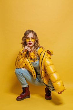 Sarı kışlık ceketli, parlak sarı arka planda mükemmel bir kadın.