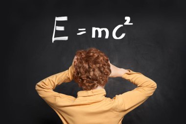 Küçük çocuk tahtada bilimsel formüle bakıyor.