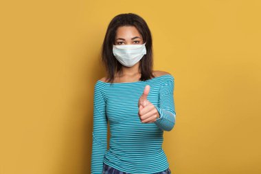 İyimser siyahi kadın, parlak sarı arka planda baş parmağını gösteriyor.