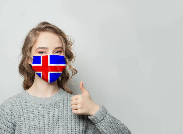 国旗アイスランドを背景に親指を立てるフェイスマスクの幸せな女性 インフルエンザの流行とウイルス保護の概念 — ストック写真