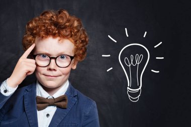 Tahta arka planda ampulü olan gözlüklü zeki çocuk.