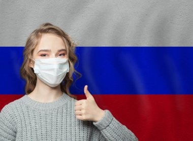 Yüzü maskeli mutlu kadın Rus bayrağında baş parmak kaldırıyor. Grip salgını ve virüs koruma kavramı