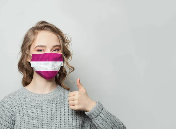 Šťastná Žena Masce Drží Palec Nahoru Vlajkou Lotyšska Pozadí Epidemie — Stock fotografie