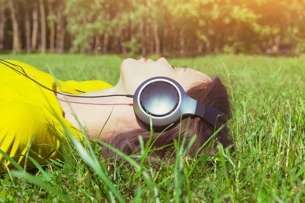 Симпатичная девушка лежит в летней траве с наушниками, слушая м — стоковое фото