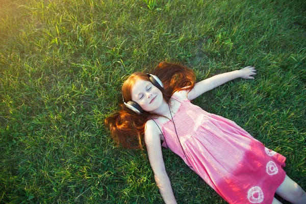红发女孩戴着耳机听音乐。从上面查看 — 图库照片