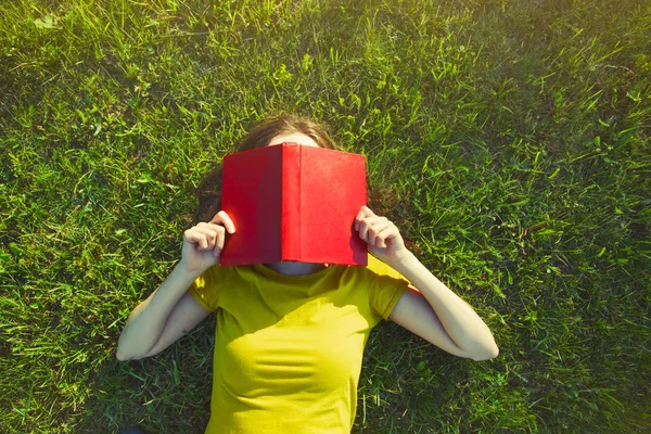 Дівчина читає книгу, що лежить у теплій літній траві. вид зверху — стокове фото