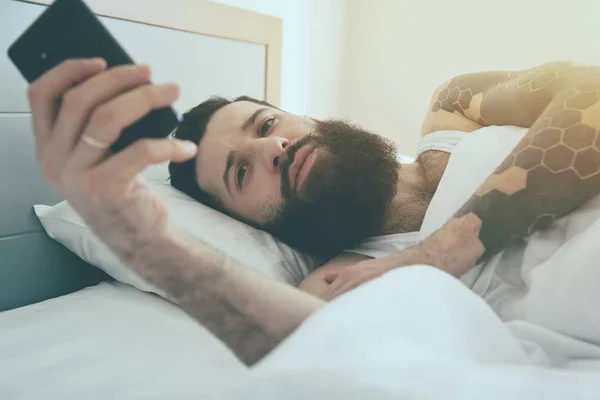 Szakállas férfi, az ágyban reggel telefon — Stock Fotó