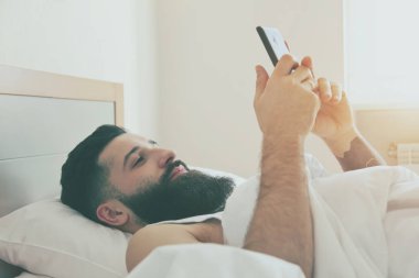 Telefon ile yatakta yatan sakallı adam