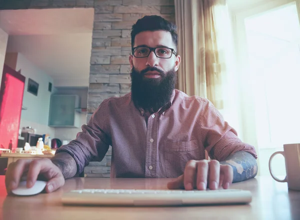 Бородатый человек, работающий с компьютером дома в качестве фрилансера — стоковое фото