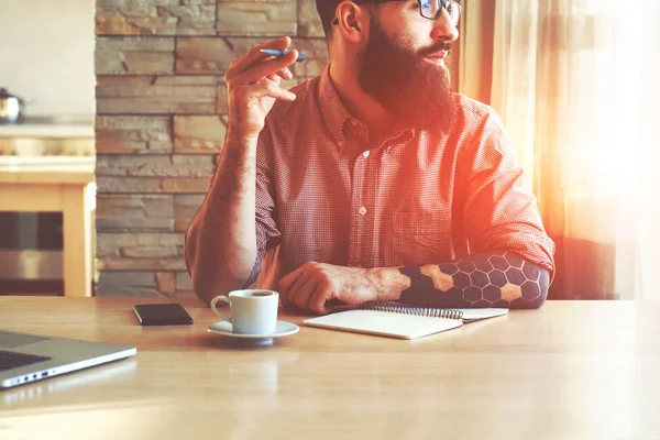 Uomo barbuto che scrive con penna nel quaderno e pensa — Foto Stock