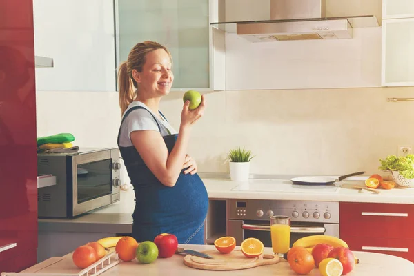 Femme enceinte mangeant des pommes dans la cuisine — Photo