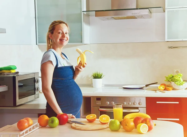 Вагітна жінка їсть банан на кухні — стокове фото