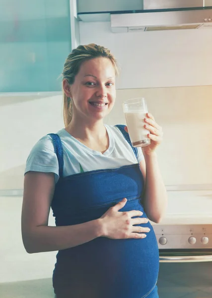 Mujer embarazada bebiendo leche en la cocina — Foto de Stock