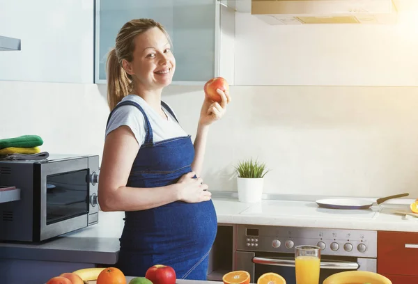 Femme enceinte mangeant des pommes dans la cuisine — Photo