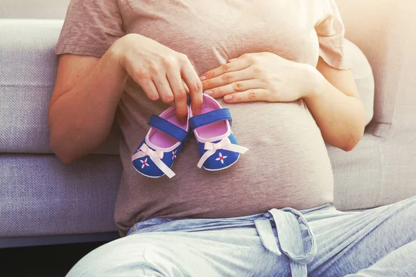 Mujer embarazada sosteniendo zapatos de bebé — Foto de Stock