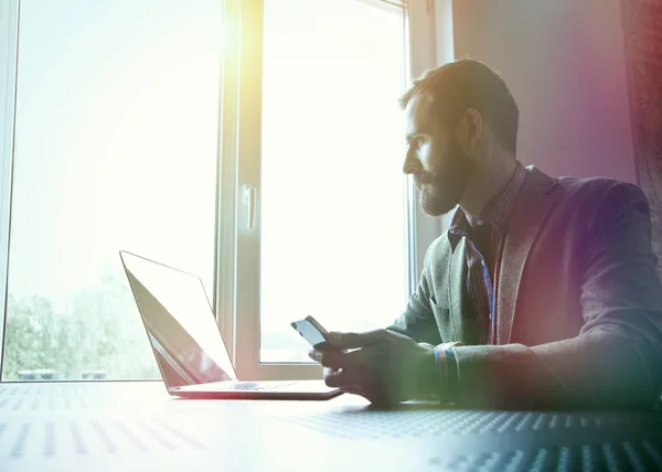 Uomo barbuto che lavora con laptop e telefono — Foto Stock