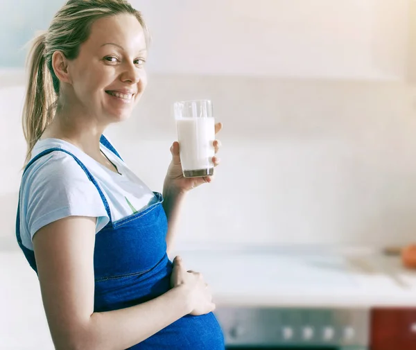 Mujer embarazada bebiendo leche en la cocina — Foto de Stock