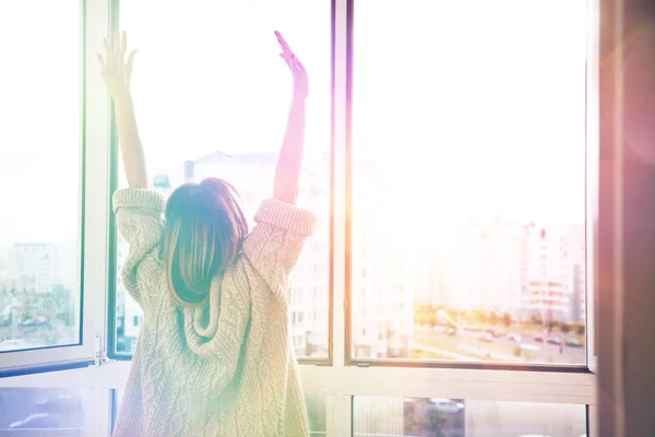 Vrouw verhogen handen in de buurt van windows — Stockfoto