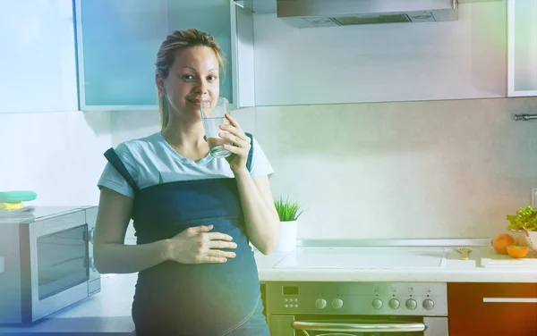 Těhotná žena pít čistou vodu v kuchyni — Stock fotografie
