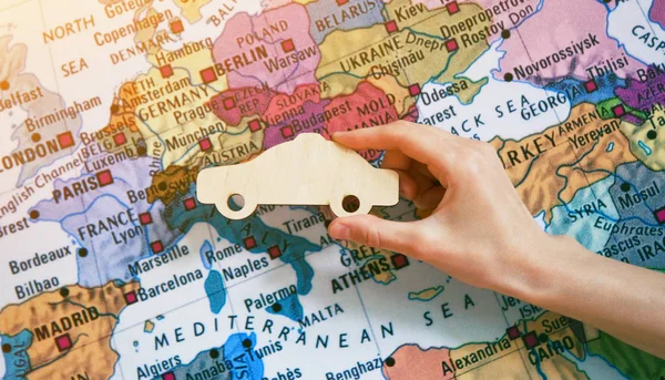 Hand with wooden car sign on world map