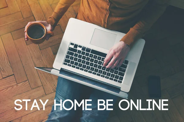 Dizüstü bilgisayar ve kahve fincanı kızların elinde, yerde oturuyor ve mesaj atıyor. Evde kal, çevrimiçi ol. Coronavirus covid-19 salgını sırasında ev izolasyonu ve karantina.