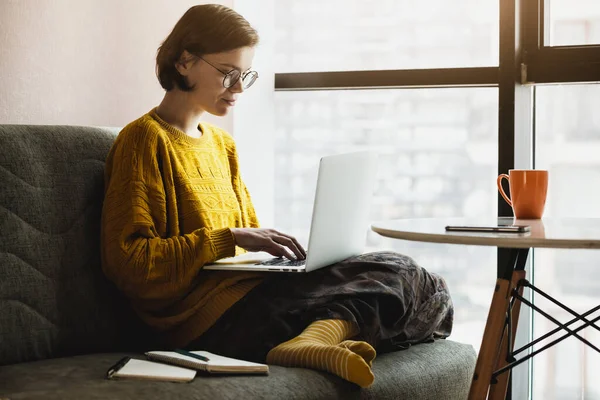 Woman working with laptop at home quarantine. Comfortable workplace with coffee on couch. Stay at home campaign