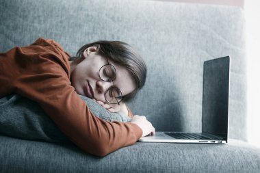 Kadın evde çalışırken dizüstü bilgisayarın yanında uyuyor ve rüya görüyor. Koltukta uzanan rahat bir iş yeri. Uzaklık çevrimiçi eğitim