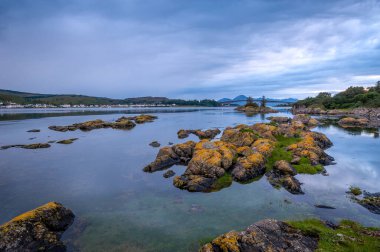 Günbatımı deniz manzarası, suda kayalar ve arkada Skye adası..