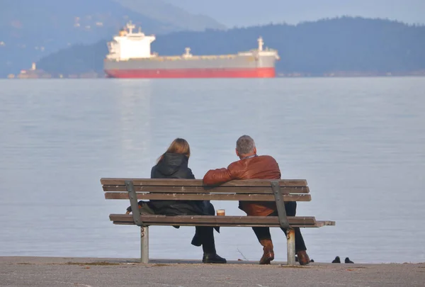 Ζευγάρι κάθεται σε ένα παγκάκι με θέα στον ωκεανό — Φωτογραφία Αρχείου