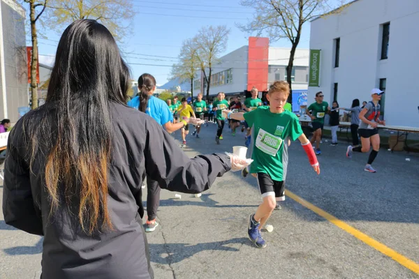 志愿者向参加2018年在加拿大温哥华的跑步者发出水 在2018年4月22日 — 图库照片