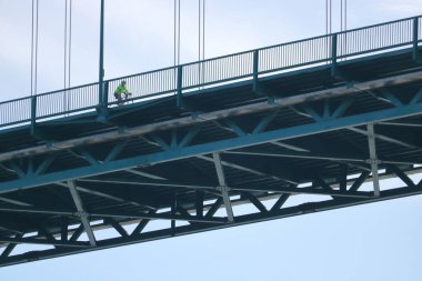 A cyclist high above as he crosses the Lions Gate Bridge, a landmark suspension bridge in downtown Vancouver, Canada on May 8, 2018. clipart