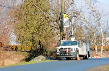 Wide view of a professional linesman using a bucket lift and specialized equipment to repair damaged lines on a telephone poll.  clipart