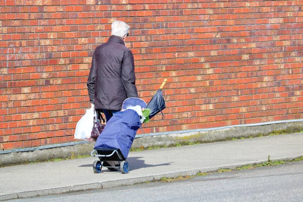 Anciano Camina Junto Una Pared Roja Ladrillo Mientras Lleva Bolsas — Foto de Stock