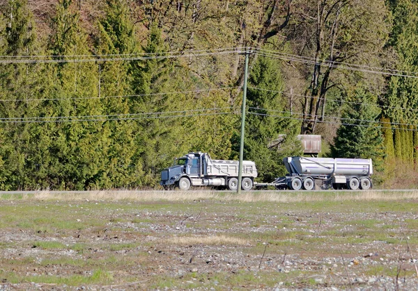 田舎道を右から左へ二つ目の荷を引く産業用ダンプトラックの広い眺め — ストック写真