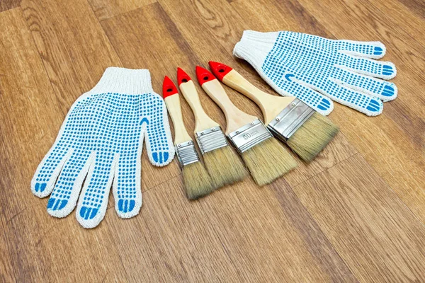 Composition from painting tools with paint brushes, gloves and paint roller on the wooden background