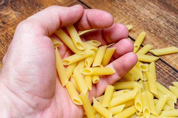 hand holding spaghetti, macaroni, pasta, linguine durum wheat Italian thin long on wooden background close up selective focus