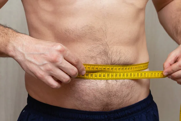 man measures the waist with a yellow tape. Diet fitness concept.