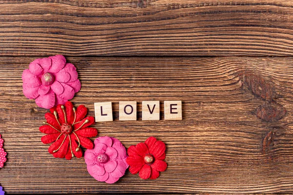 Word love with hearts and flower on the brown wooden background. Valentine gift card background