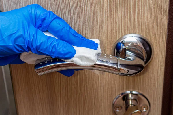cleaning, disinfecting, wiping the chrome door handle with a hand in glove and napkin close up