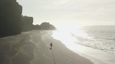 Deniz kenarında yürüyen adam sahilde sörf yapar.