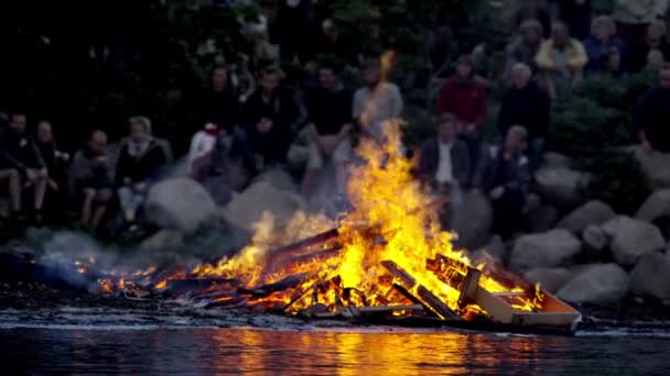 Colpo medio di un mucchio di legna che brucia con fiamme alte vicino alla riva del fiume — Video Stock