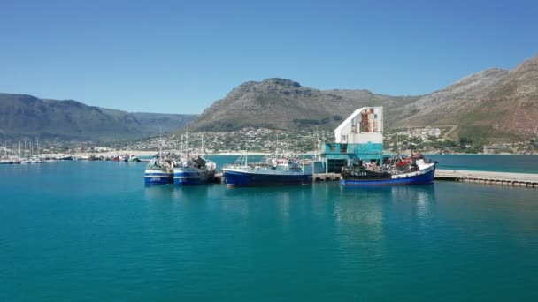 Rıhtıma yanaşmış balıkçı tekneleri ve sıradağlarla limanın üstünde uçan drone. — Stok video