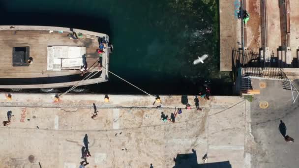 Blick von oben auf ein Boot, das an einen Hafen gebunden ist und Menschen, die am Weg schwimmen und gehen — Stockvideo
