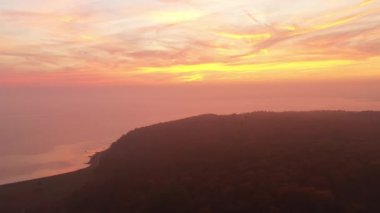 Okyanus üzerindeki bulutların ve ormanın sonundaki güneşin doğuşundaki sahilin görüntüsü.