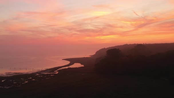 Volando por encima de la orilla bajo un cielo de color naranja durante una marea baja al amanecer — Vídeos de Stock