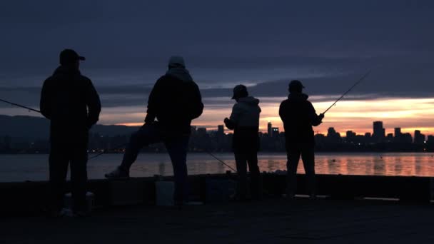 Quatre silhouettes d'hommes ligne de pêche par un quai en bois sous un ciel orange — Video