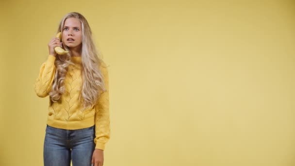 Γυναίκα σε ένα κίτρινο πουλόβερ έχοντας μια συνομιλία σε ένα τηλέφωνο μπανάνα τότε πέφτει — Αρχείο Βίντεο