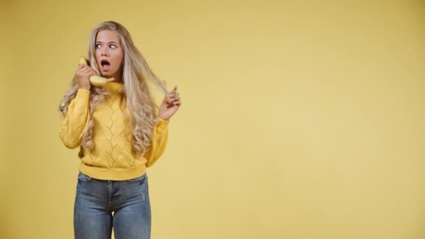 Giocoso donna bionda in maglione giallo che tiene una banana alle orecchie — Video Stock