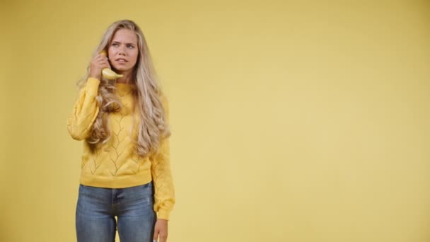 Блондинка с беспокойным лицом, разговаривая с спелым банановым телефоном — стоковое видео