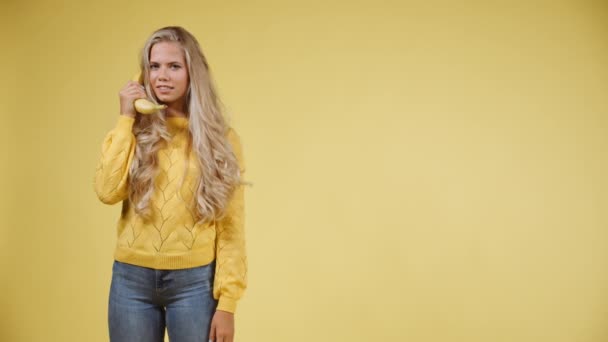 Een model met lang blond haar praten op een banaan telefoon en vervolgens acteren geschokt — Stockvideo